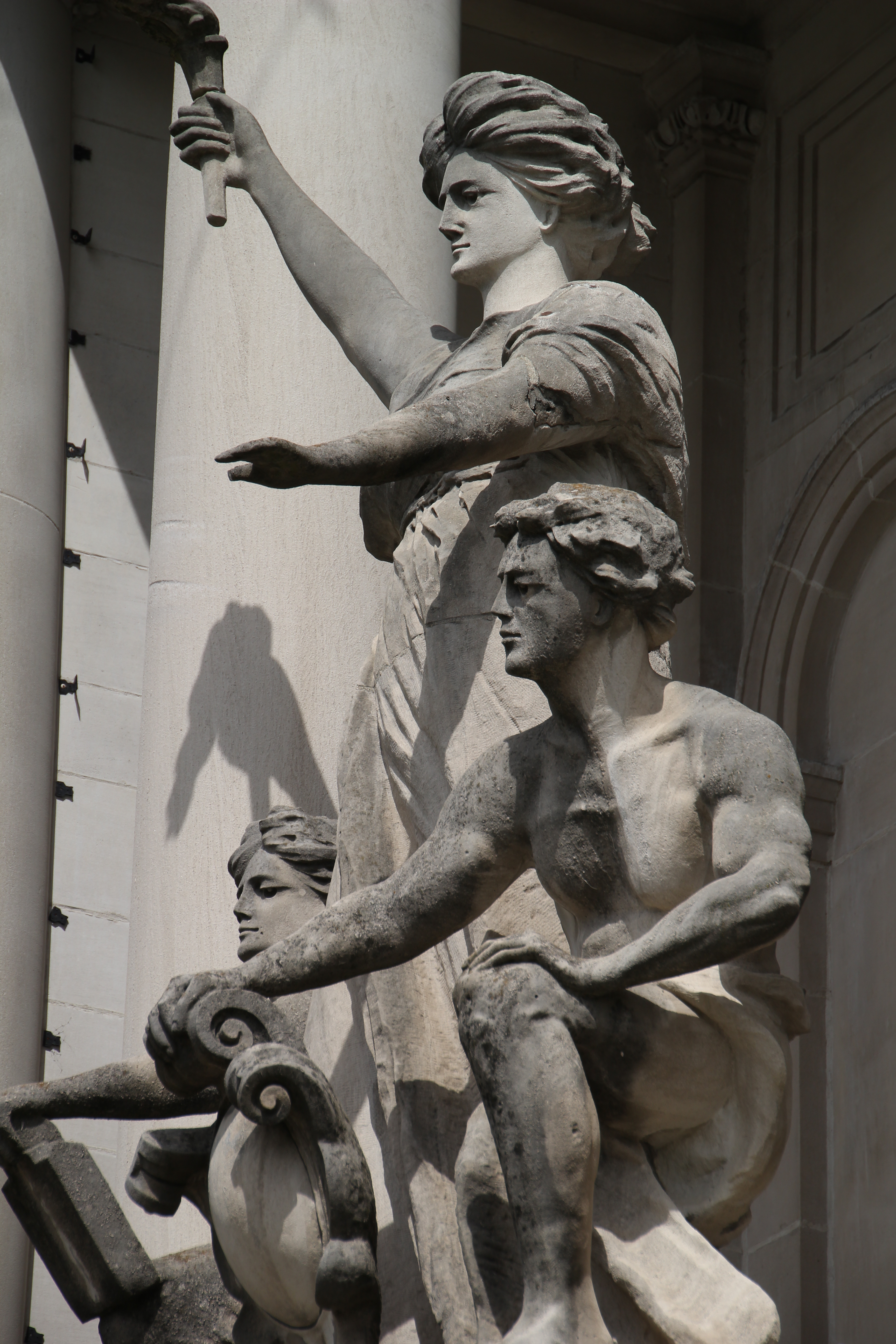 photo of classical style statues: a woman holds a torch, flanked by two crouching men