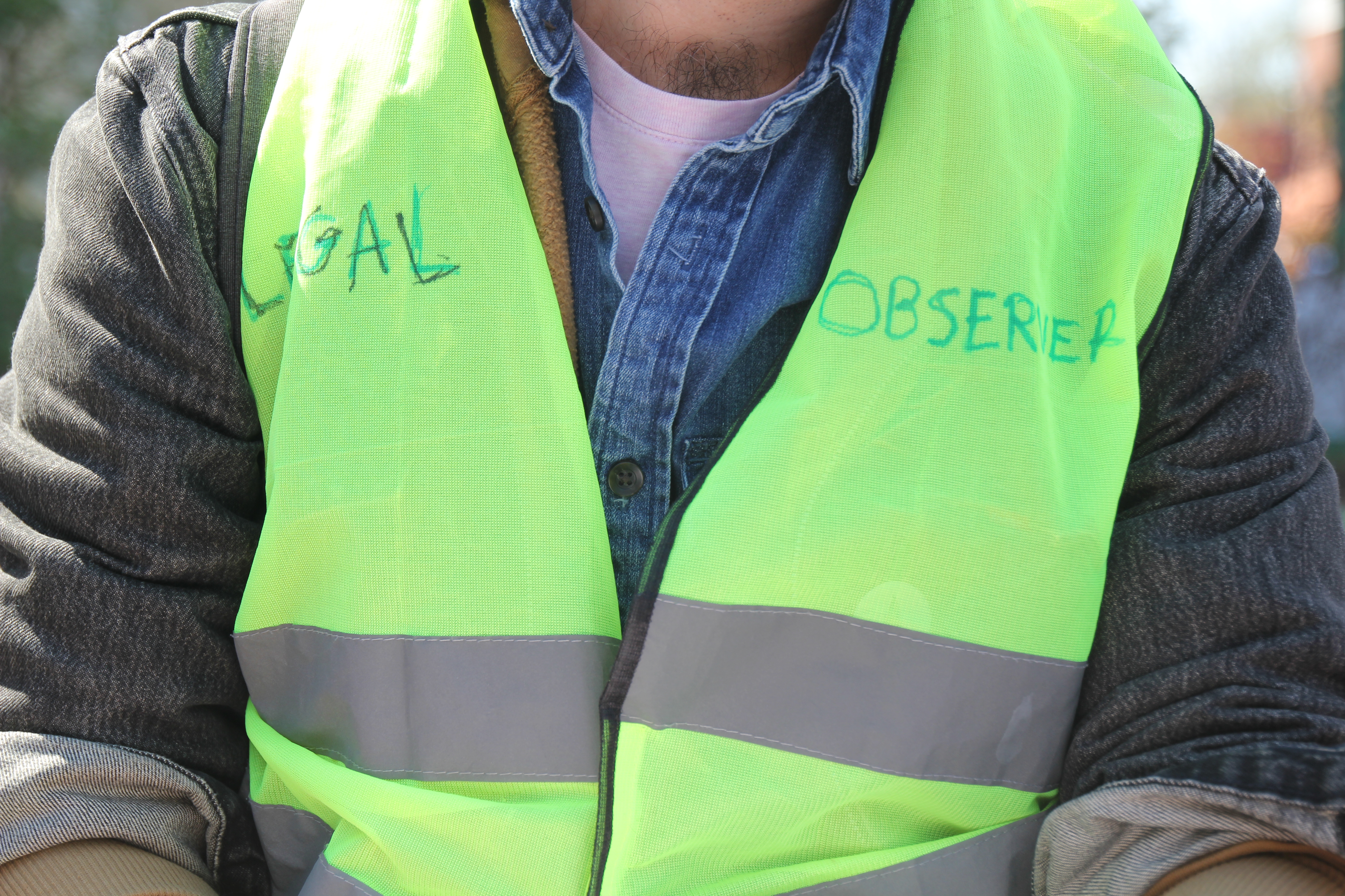a man wearing a jean jacket with a neon green safety vest on. the safety vest says legal observer