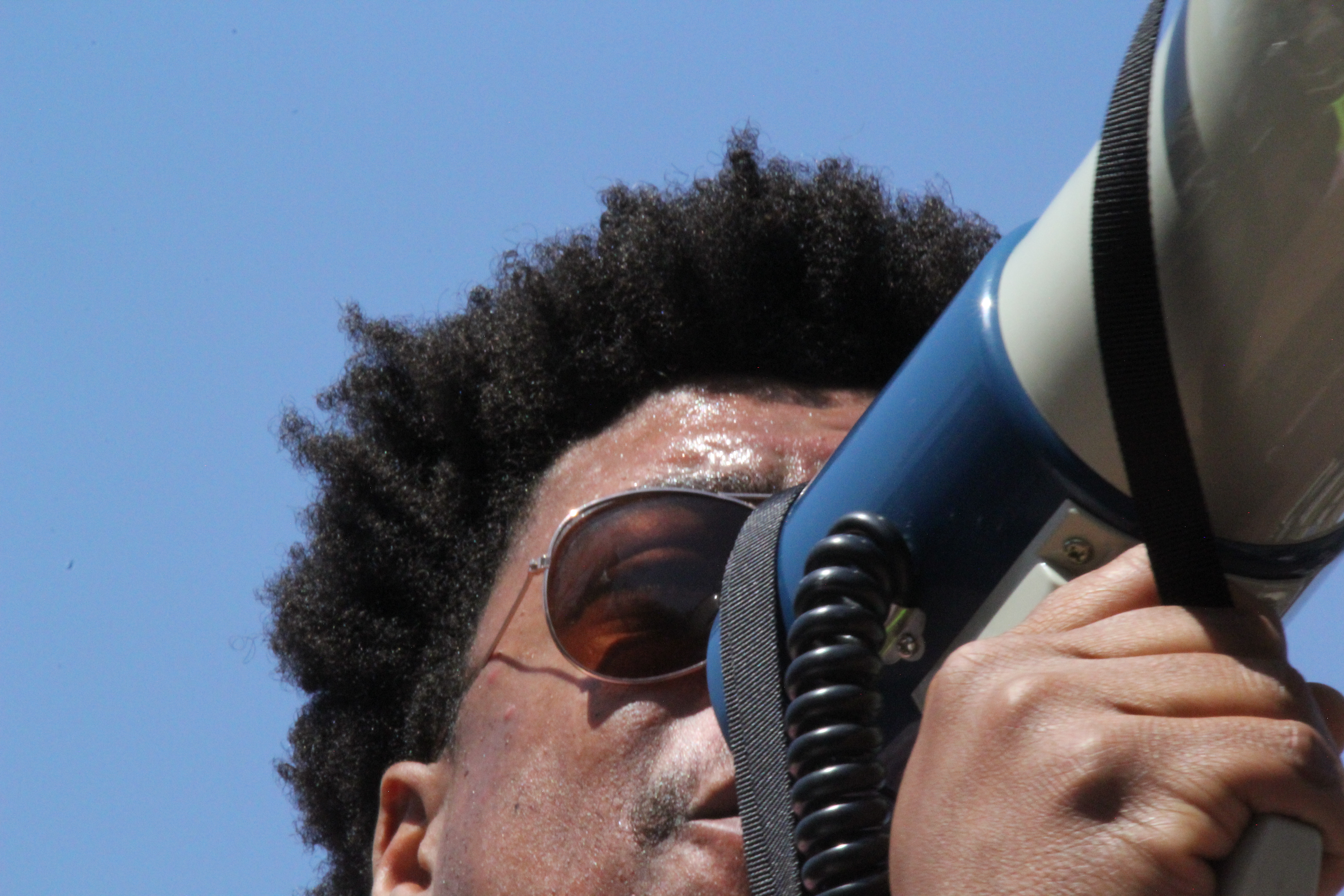 close up of a man holding a megaphone. he has tight coiled hair and sunglasses